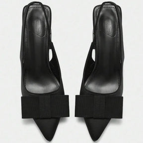 Detalhe do laço e da tira do scarpin slingback preto. A imagem aproxima a textura do material em couro PU e o acabamento sofisticado do acessório.