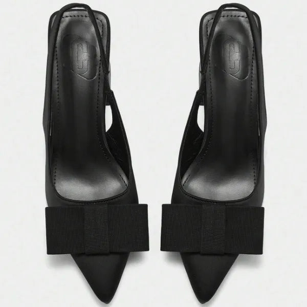 Detalhe do laço e da tira do scarpin slingback preto. A imagem aproxima a textura do material em couro PU e o acabamento sofisticado do acessório.