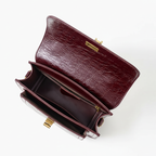 Bolsa crossbody feminina couro vinho aberta por cima, com forro, espaço interno e fechamento visíveis, sobre fundo claro