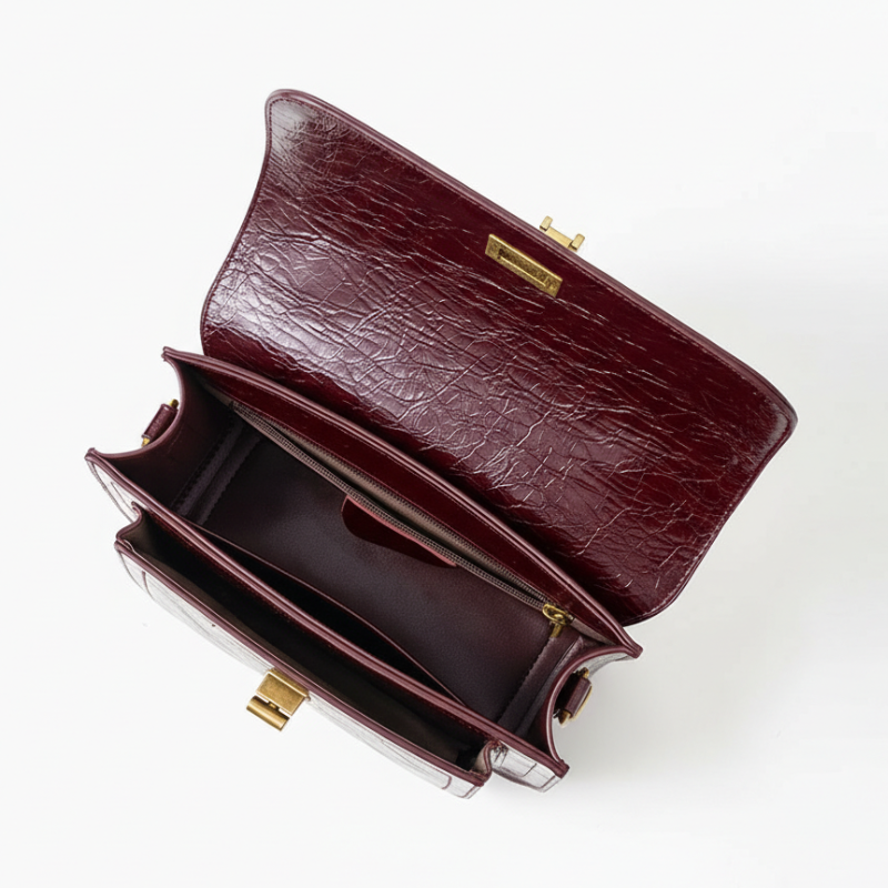 Bolsa crossbody feminina couro vinho aberta por cima, com forro, espaço interno e fechamento visíveis, sobre fundo claro