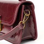Bolsa crossbody feminina couro vinho em ângulo três-quartos, mostrando formato, volume e alça, sobre fundo claro