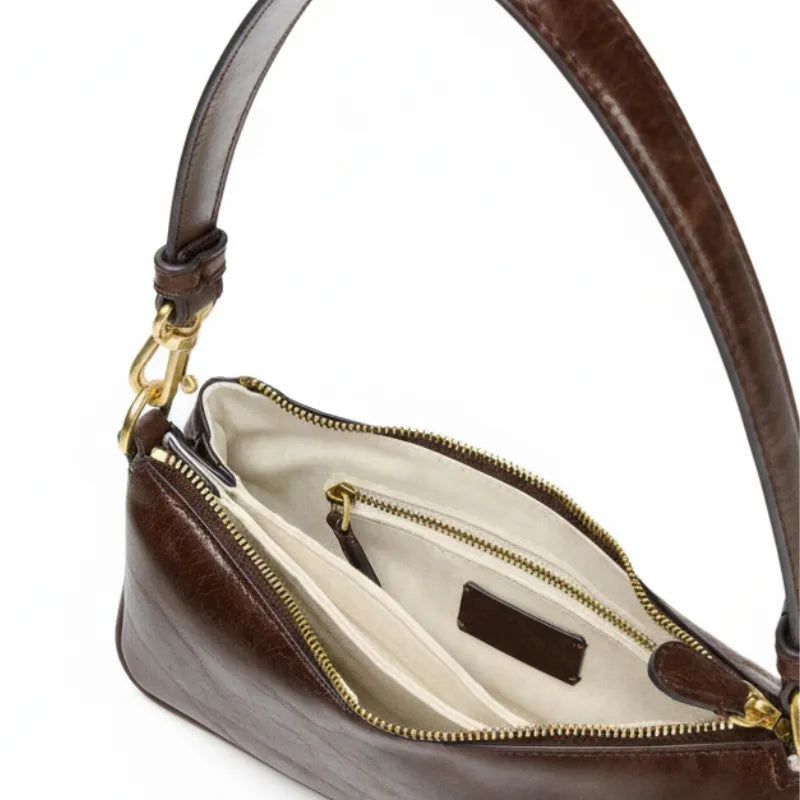 Bolsa de ombro baguete marrom aberta por cima, com forro, espaço interno e fechamento visíveis, sobre fundo claro