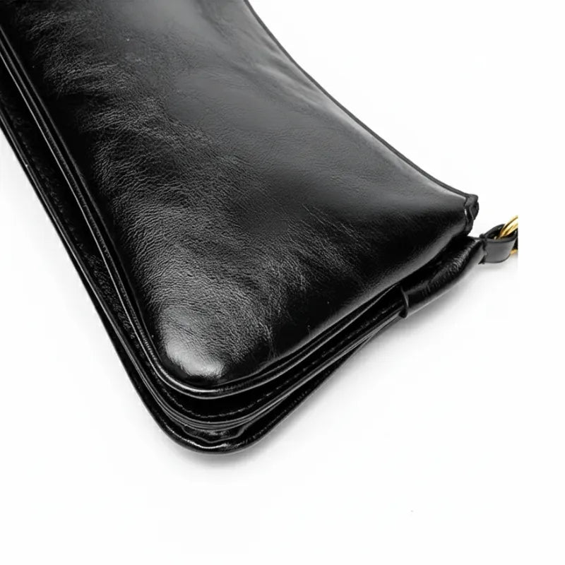 Bolsa de ombro baguete preta em perspectiva lateral oposta, com volume e estrutura visíveis, sobre fundo claro