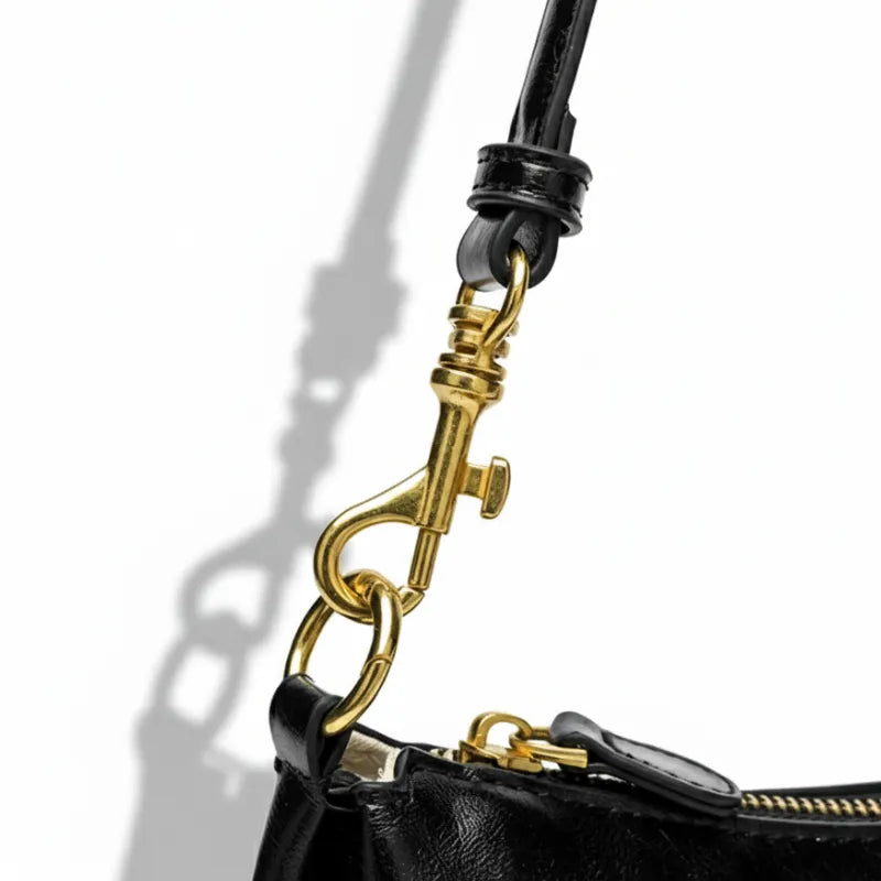 Bolsa de ombro baguete preta em close no fecho e nas ferragens, com textura e brilho em destaque, sobre fundo claro