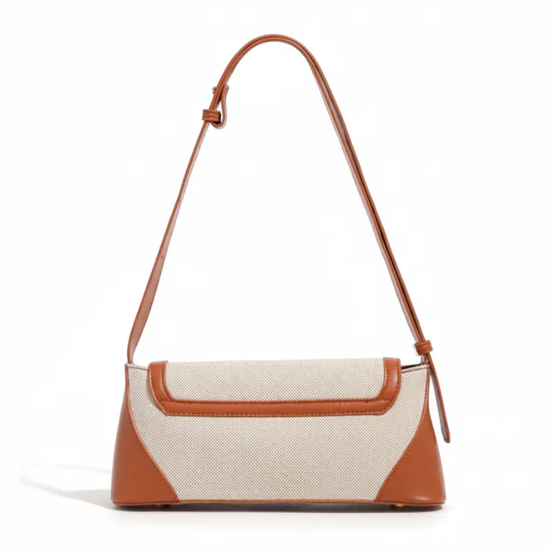 Bolsa de ombro marrom canvas trava dourada em ângulo três-quartos, mostrando formato, volume e alça, sobre fundo claro