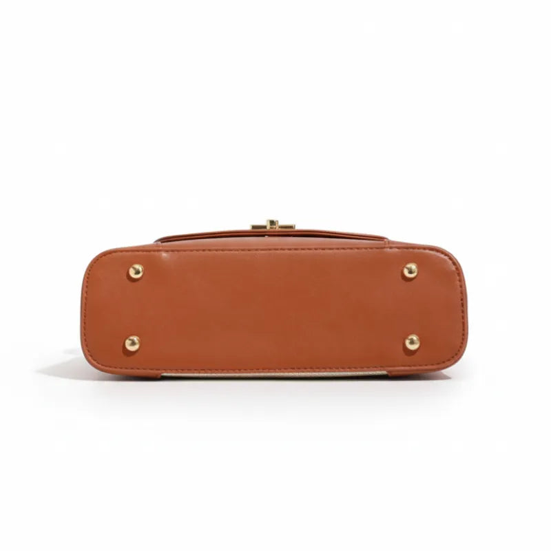 Bolsa de ombro marrom canvas trava dourada vista pela base, com fundo, pés metálicos e bordas em destaque