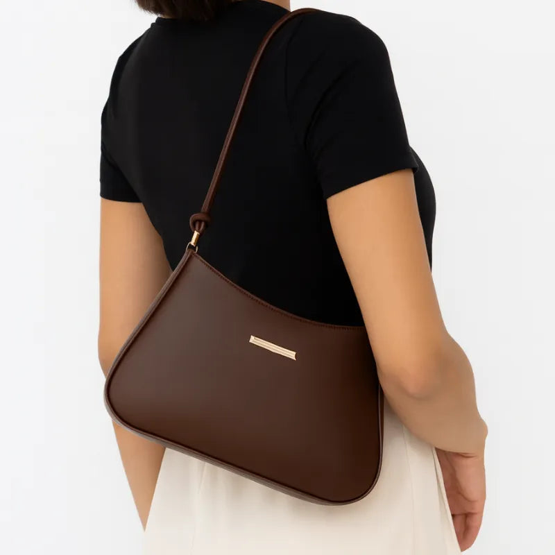 Bolsa de ombro marrom com alça de nó usada no ombro pela modelo, mostrando proporção e caimento frontal