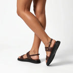 Papete marrom flatform com fivela nos pés da modelo em vista lateral, destacando perfil e altura, sobre fundo claro