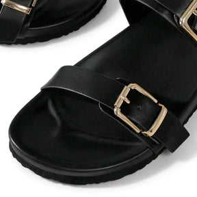 Papete casual preta com duas tiras ajustáveis, fivelas douradas quadradas e acabamento premium, detalheclose-up lateral
