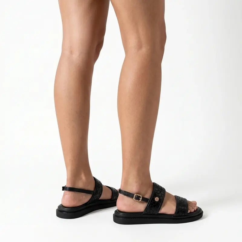 Papete preto flatform com fivela nos pés da modelo de lado, destacando tiras, fivelas e altura do solado
