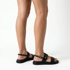 Papete preto flatform com fivela nos pés da modelo de lado, destacando tiras, fivelas e altura do solado