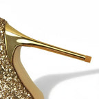 Scarpin dourado salto alto com glitter em vista traseira, com calcanhar, salto e acabamento da sola visíveis