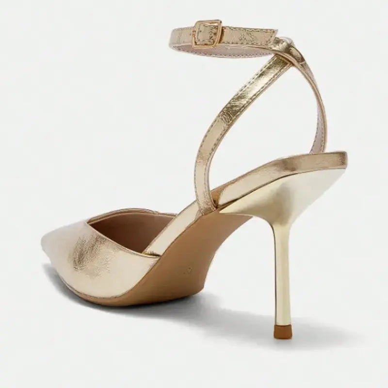 Scarpin dourado slingback bico fino nos pés da modelo em vista frontal, mostrando ajuste e proporção, sobre fundo claro