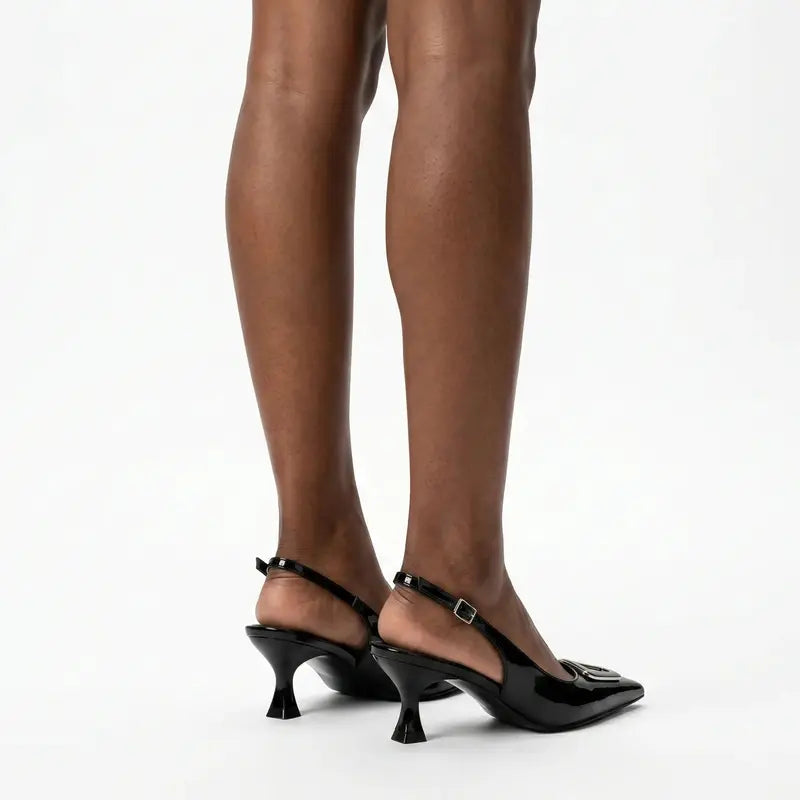 Scarpin preto slingback com detalhe geométrico nos pés da modelo em vista traseira, mostrando ajuste e acabamento