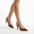 Scarpin slingback castanho verniz salto médio nos pés da modelo em vista frontal, mostrando ajuste e proporção