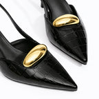 Scarpin slingback preto croco detalhe dourado em close no bico, tiras ou fivela, com textura e metal em destaque